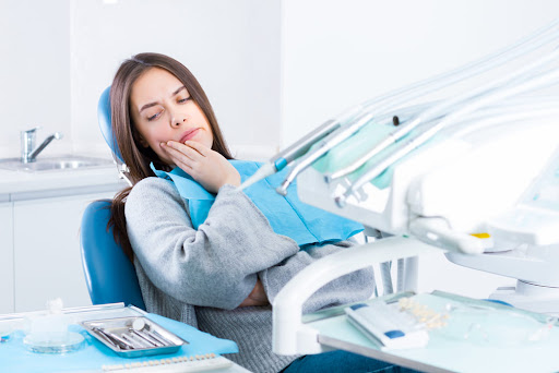Lady at the dentist holding her jaw in discomfort.