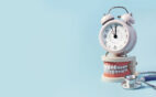 A model of human teeth with a clock on top next to a stethoscope to symbolize “how long does wisdom teeth removal take”